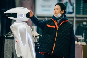 A woman wearing a face mask interacts with a store assistant robot